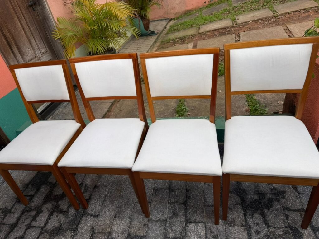 Quatro cadeiras de jantar de madeira com assentos e encostos estofados em tecido branco.