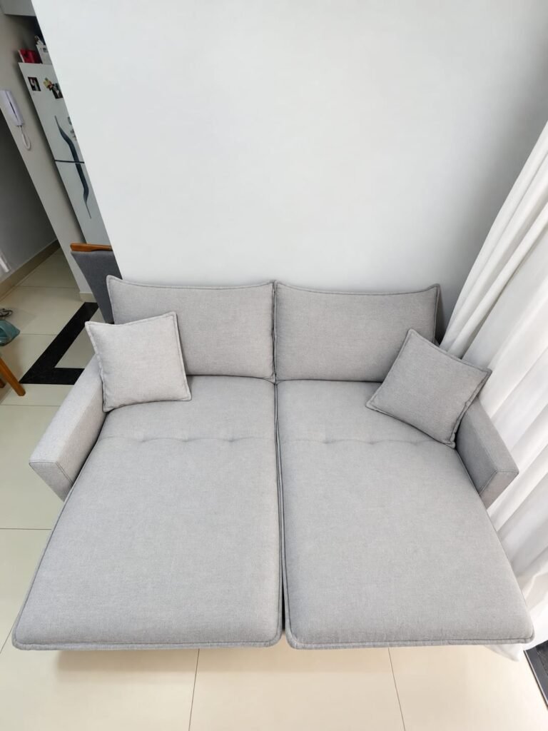 Sofá retrátil cinza-claro de dois lugares com assentos estendidos e almofadas, em ambiente residencial.