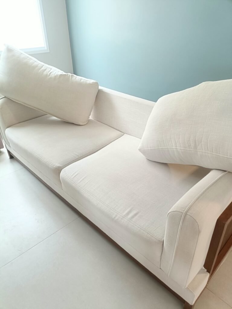 Sofá de dois lugares em tecido branco off-white com almofadas soltas, em ambiente residencial.
